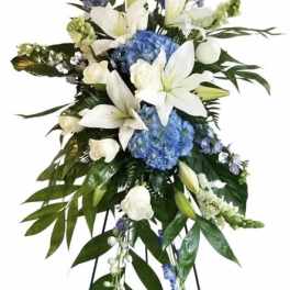 Standing floral spray with white lilies, blue hydrangeas, and an easel