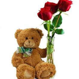 Teddy bear beside a glass vase with three red roses