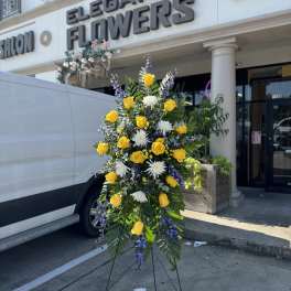 Standing floral spray with yellow roses, white blooms, and purple accents