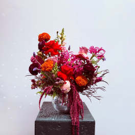 Bright mixed bouquet in a mirrored vase with red, pink, and orange blooms