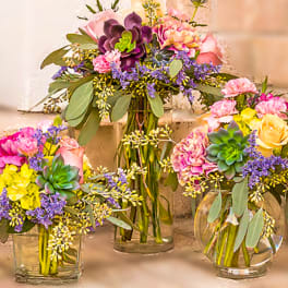 Three colorful floral arrangements in glass vases with succulents