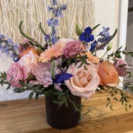 Mixed bouquet of pink and peach roses with blue flowers in a dark vase