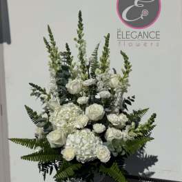White floral arrangement in a vase with tall greenery and roses