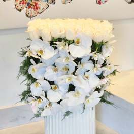 White roses and orchids arranged in a ribbed white vase