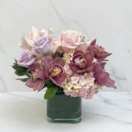 Pink and lavender flowers arranged in a square glass vase