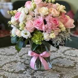 Pink and white rose bouquet in a glass vase with a pink ribbon