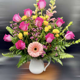 Pink roses and a peach gerbera daisy in a white pitcher vase