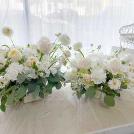 Two white floral arrangements on a table with a decorative birdcage