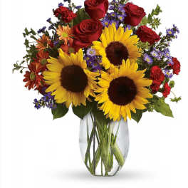 Bouquet of sunflowers, red roses, and purple daisies in a clear glass vase