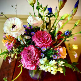 Mixed bouquet with pink roses, white ranunculus, purple iris, and small asters in a glass vase