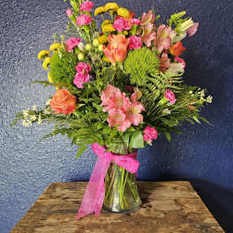 Mixed bouquet of pink, orange, and yellow flowers in a glass vase with a pink ribbon