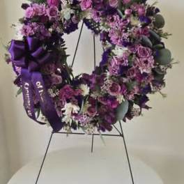 Purple floral wreath on a black stand with a ribbon bow