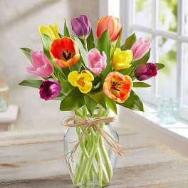 Colorful tulips arranged in a clear glass vase with a raffia bow.