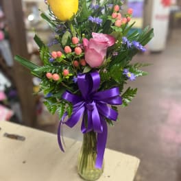 Bouquet of yellow and pink roses in a glass vase with a purple ribbon