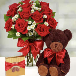 Bouquet of red roses in a glass vase with a teddy bear and chocolate box