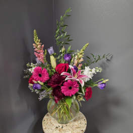 Mixed bouquet of pink, purple, white, and red flowers in a glass vase.