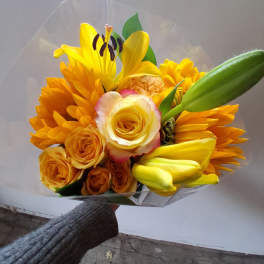 Yellow and orange bouquet with roses and lilies wrapped in clear plastic