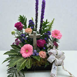 Floral arrangement with pink gerbera daisies, roses, and a cross centerpiece