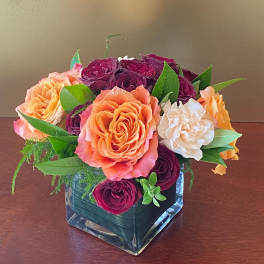 Bouquet of orange, burgundy, and white roses in a square glass vase