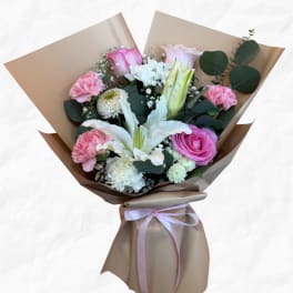 Bouquet of pink and white flowers wrapped in brown paper with a ribbon