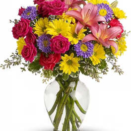 Bouquet of pink roses, lilies, and yellow daisies in a clear glass vase