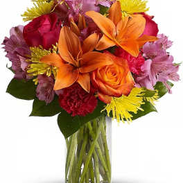 Mixed bouquet of orange lilies, roses, and colorful daisies in a glass vase