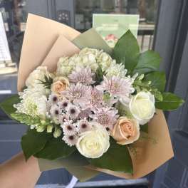 Hand-tied bouquet of white and blush flowers wrapped in tan paper