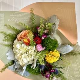 Mixed bouquet with roses, hydrangea, tulips, and yellow blooms in pastel wrapping