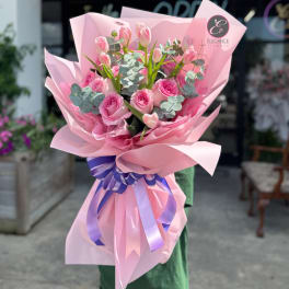 Pink rose and tulip bouquet wrapped in pink paper with a purple ribbon