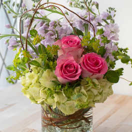 Pink roses and lavender flowers in a glass vase with curly branches
