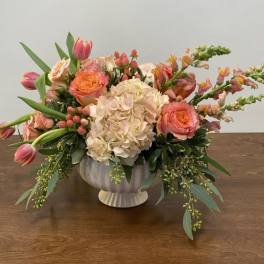 Peach and pink floral arrangement in a white pedestal vase