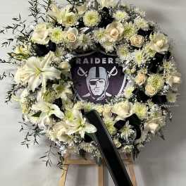 White floral funeral wreath on an easel with a black ribbon