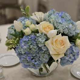 Blue hydrangeas and cream roses in a clear glass vase