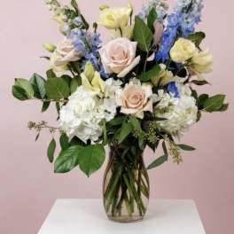 Mixed bouquet of pastel roses, hydrangeas, and blue delphinium in a glass vase
