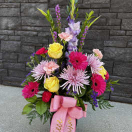 Colorful standing floral arrangement with pink ribbon in a black container