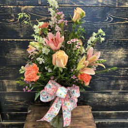 Mixed bouquet of peach and pink flowers in a glass vase with a floral ribbon