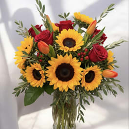 Bouquet of sunflowers, red roses, and orange tulips in a glass vase