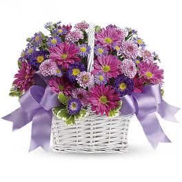 Purple and pink daisy bouquet in a white basket with lavender ribbon