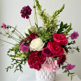 Mixed bouquet of pink, white, and purple flowers in a white vase