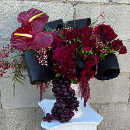 Deep red floral arrangement with anthuriums and roses in a white pedestal vase