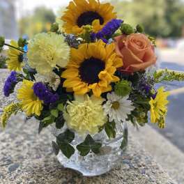 Mixed bouquet in a clear glass vase with sunflowers, a peach rose, and carnations