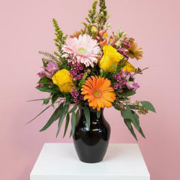 Mixed bouquet in a black vase with pink, yellow, and orange blooms