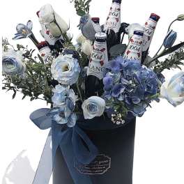 Blue and white flowers arranged with beer bottles in a black hatbox.
