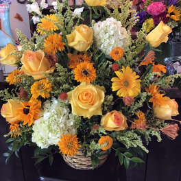 Basket arrangement of yellow roses, orange daisies, and white hydrangeas