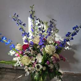 Mixed bouquet of white roses, blue delphinium, and pink flowers in a glass vase