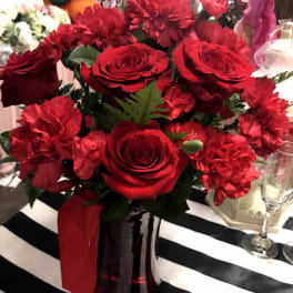 Red roses and carnations in a dark vase with a Valentine sign