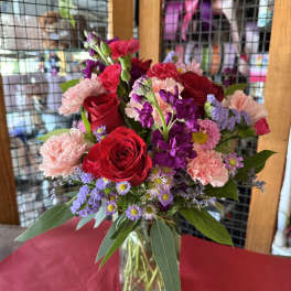 Mixed bouquet of red roses, pink carnations, and purple flowers in a glass vase