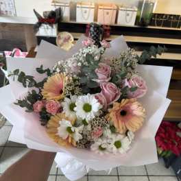 Handheld bouquet of pink roses, gerbera daisies, and white daisies wrapped in white paper
