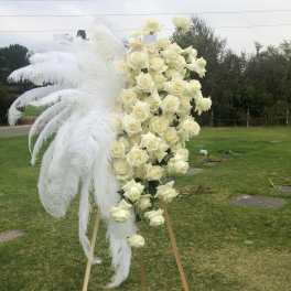 Tall white rose standing spray with large white feathers on an easel
