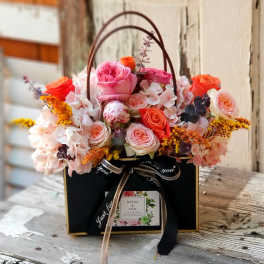 Pink and orange roses arranged in a black gift box with a handle